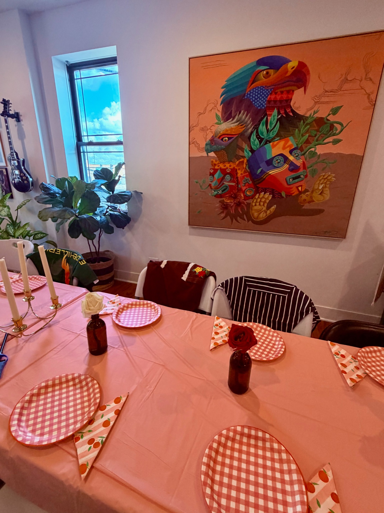 Dining table set with pink linens beneath a large colorful artwork