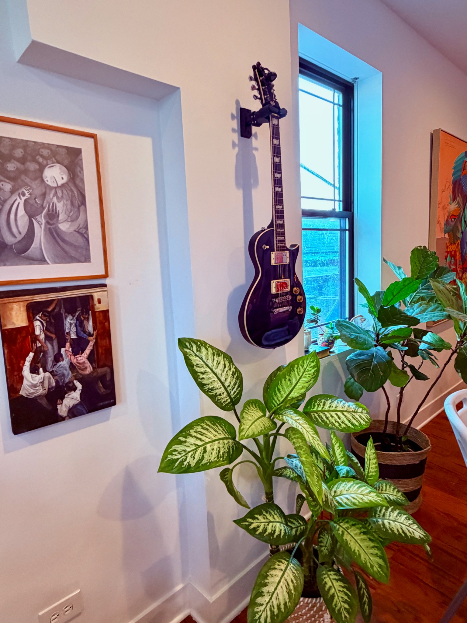 Art-filled corner with a wall-mounted guitar and lush green plants