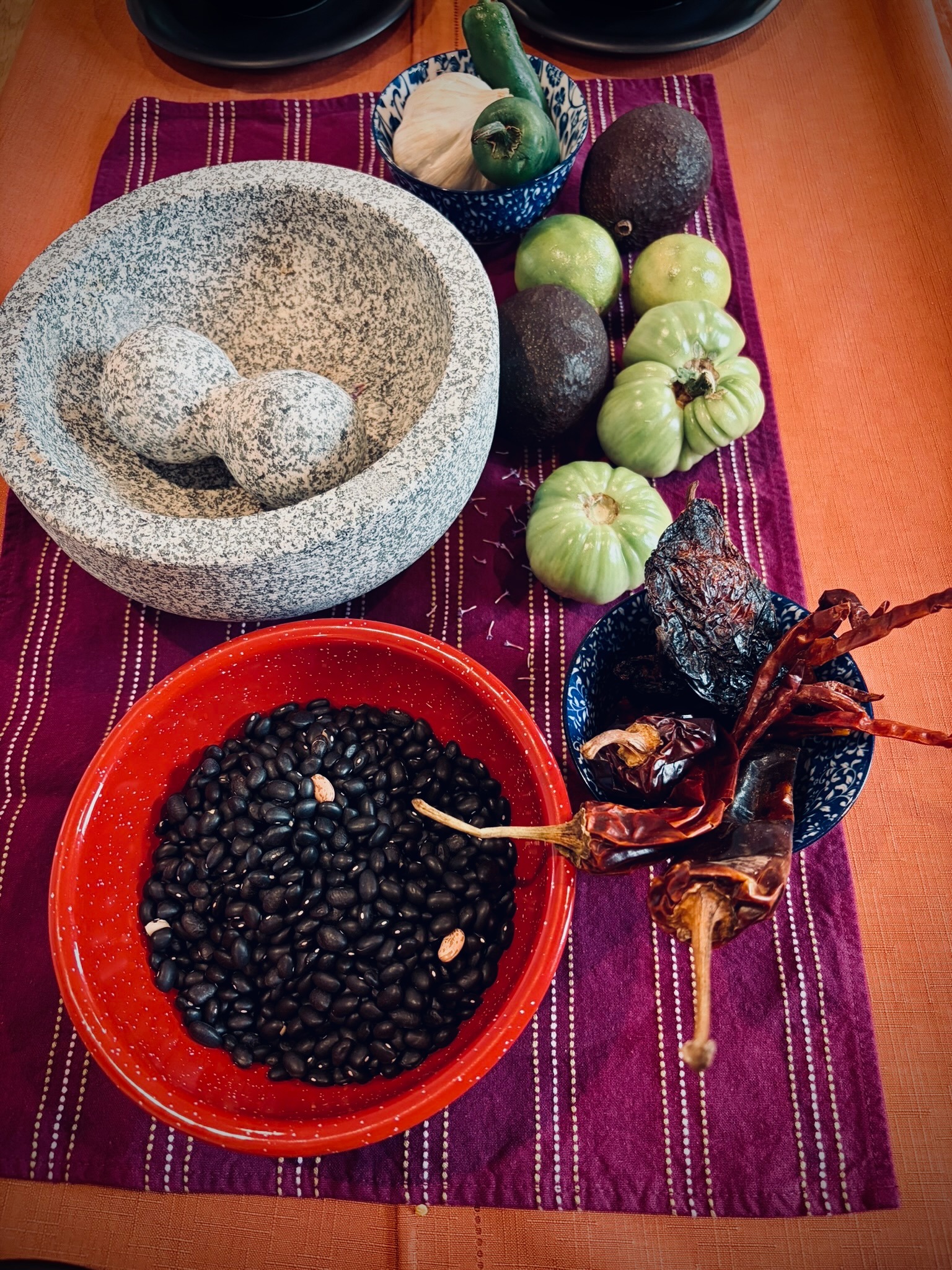 Molcajete, black beans, chiles, tomatillos, and avocados arranged on a colorful table